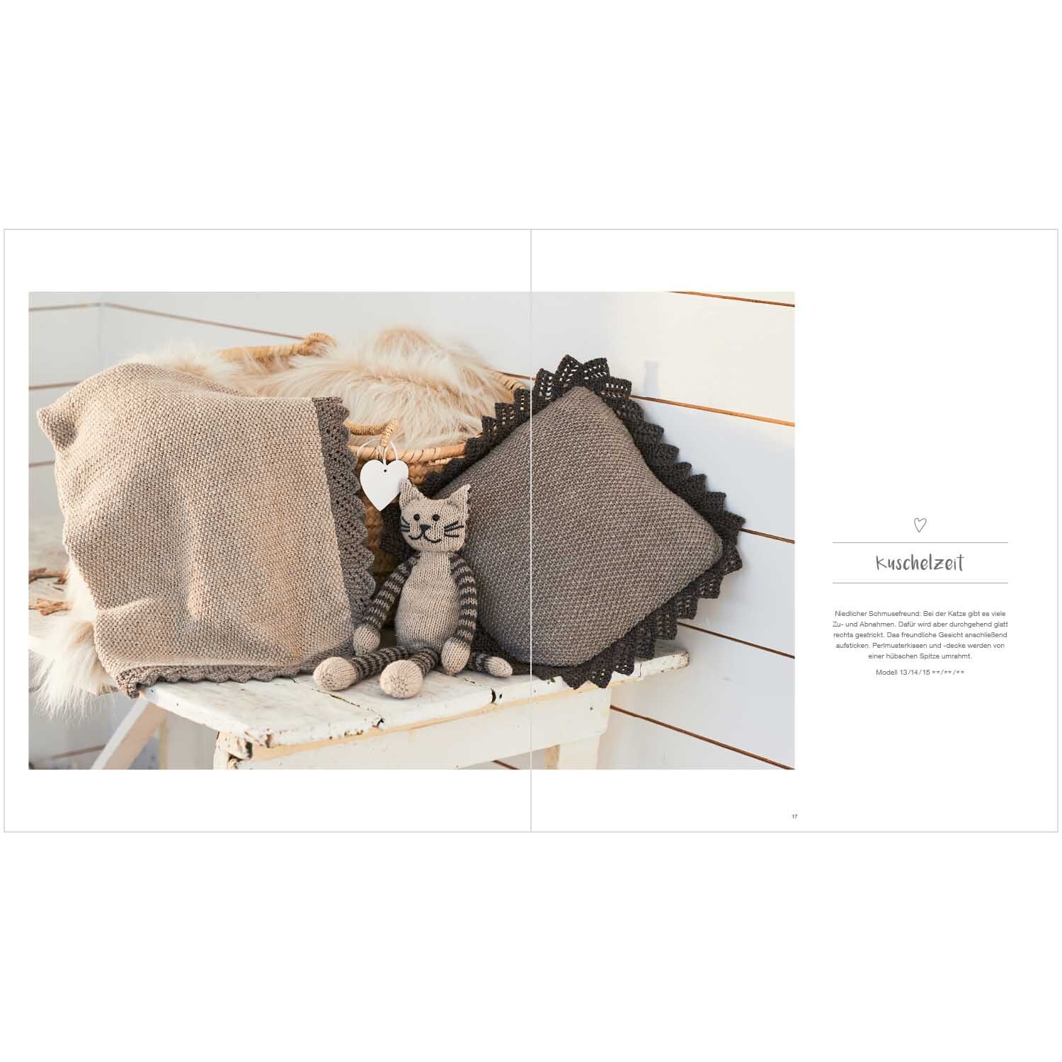 Rico Baby Heft Nr.25: Strickdecke und Kissen in Beige mit schwarzem Rand, dekoriert mit einem Stofftier auf einer Bank.