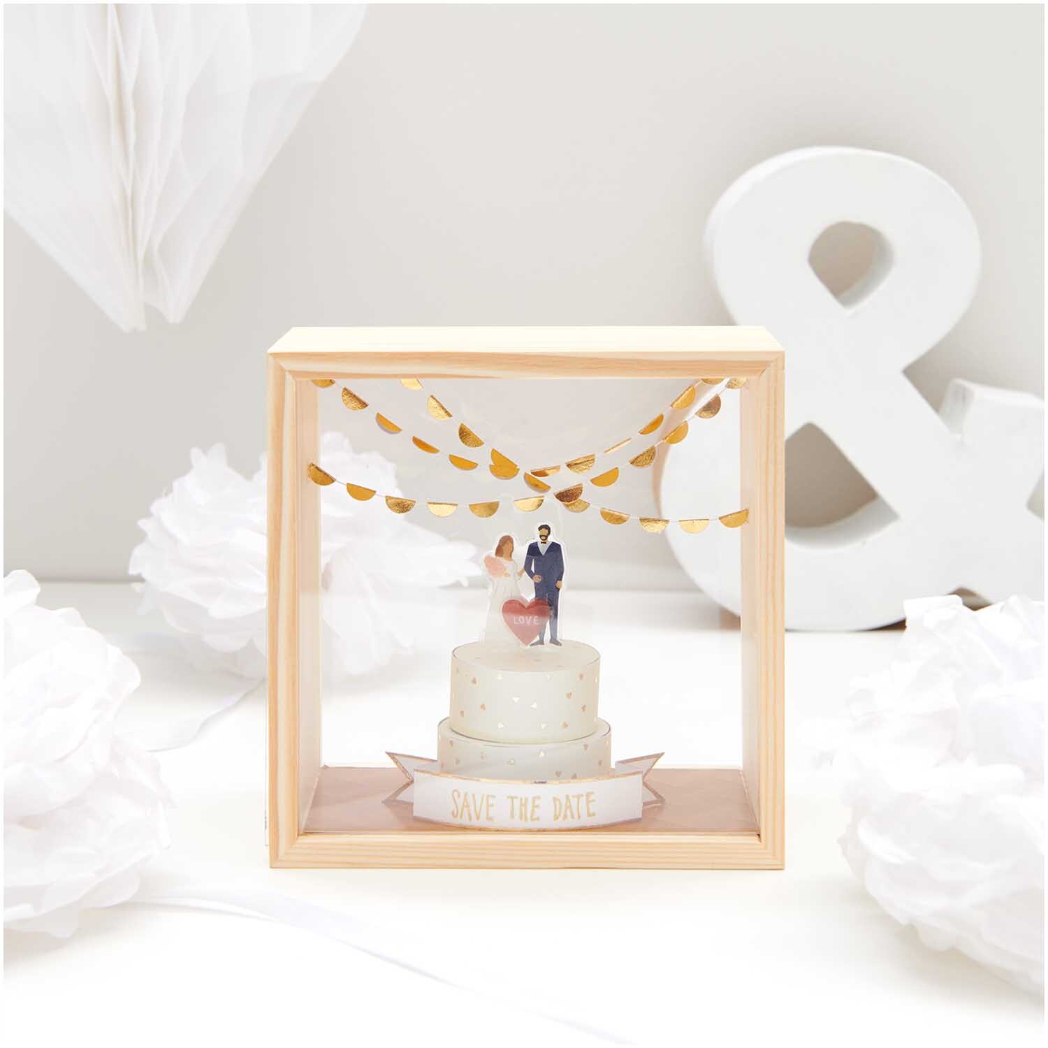 Figurico Objektkasten mit 2 Acrylscheiben zeigt Hochzeitspaar auf Torte, umgeben von goldenen Girlanden.