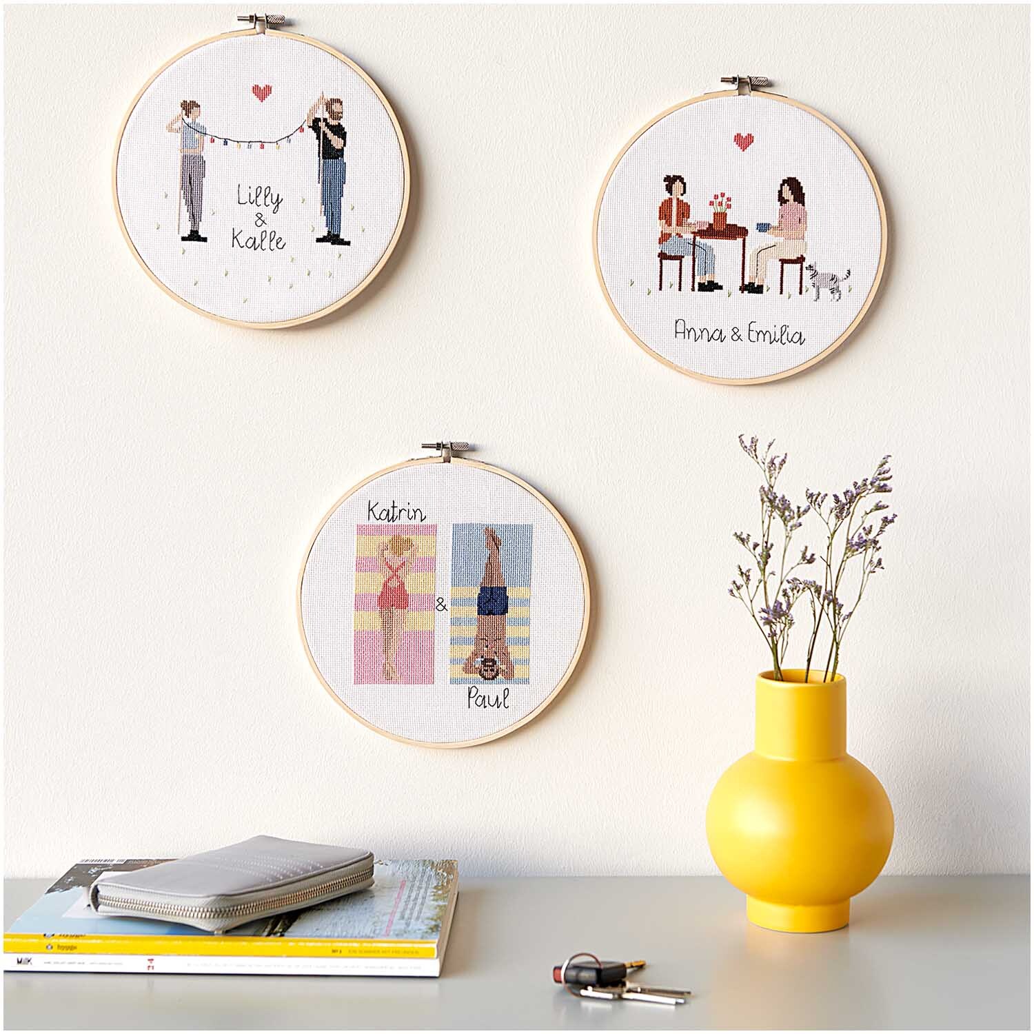 Figurico Stickpackung Teatime 20cm zeigt drei bestickte Rahmen an einer Wand, dekoriert mit einem gelben Krug und Büchern.