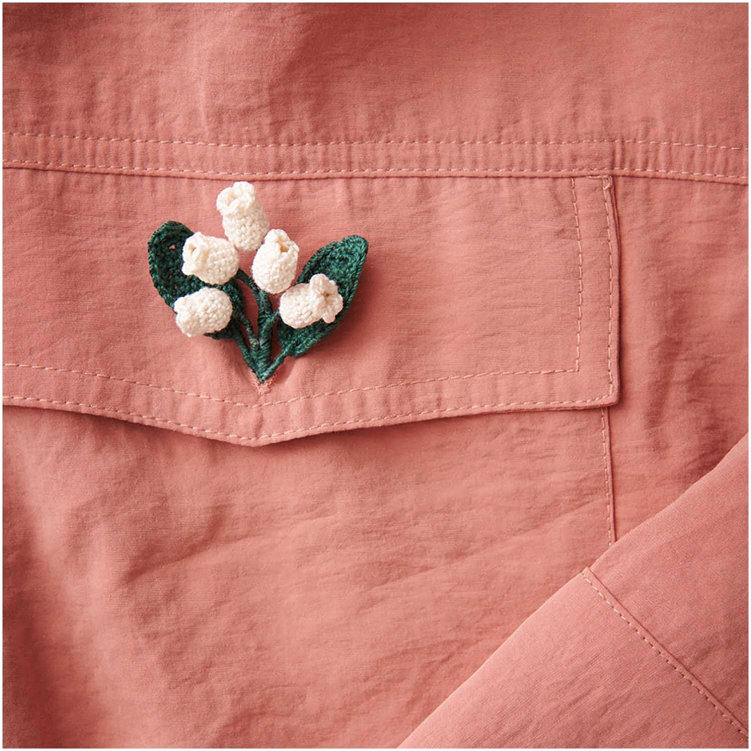 Essentials Crochet: Handgefertigte cremefarbene Häkelblume auf rosa Stoff von Rico Design.