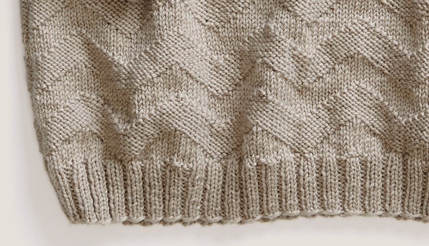 Strickanleitung Pullover aus Essentials Soft Merino aran zeigt ein gestricktes Zickzackmuster in Beige. Ideal für stilvolle, warme Kleidung.