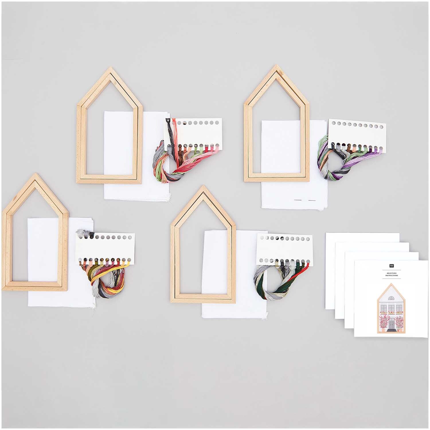 Stickpackung 4 Jahreszeiten mittel zeigt Holzrahmen, Garn und Anleitungen von Rico Design auf grauem Hintergrund.