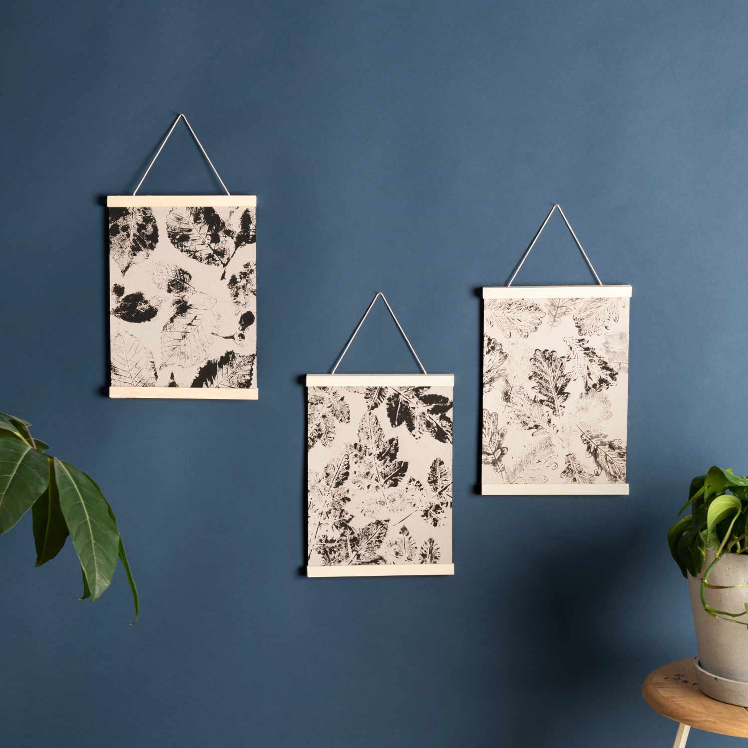 Anleitung Bilder mit Acrylfarbe und echten Blättern stempeln: Drei gerahmte Kunstwerke an blauer Wand, inspiriert von Naturmotiven.