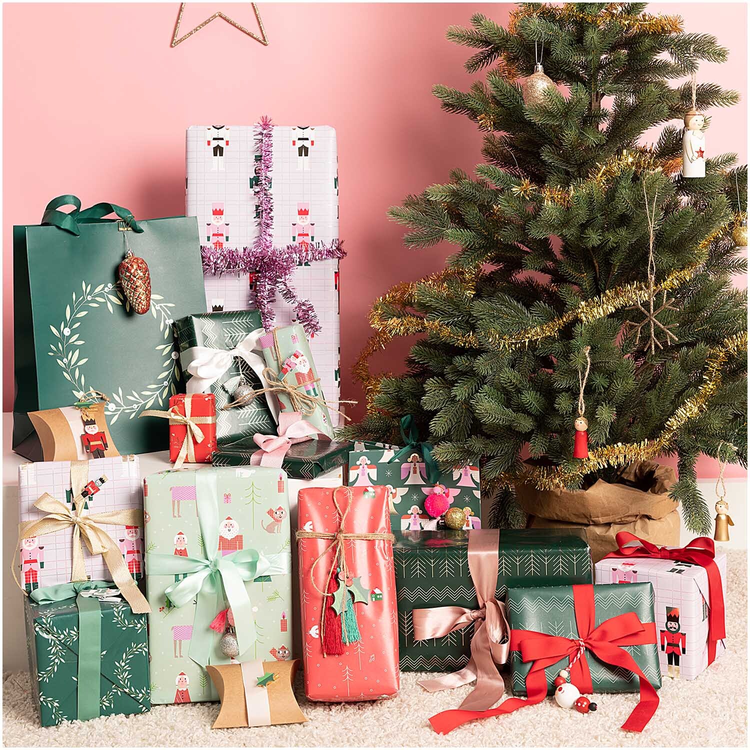Paper Poetry Geschenkpapier zeigt festlich verpackte Geschenke in verschiedenen Designs neben einem Weihnachtsbaum.