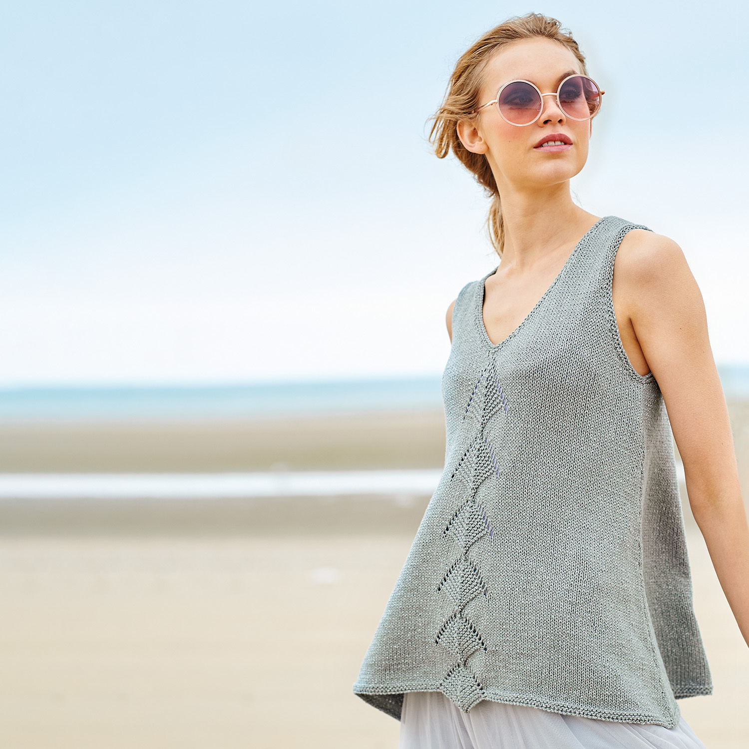 Strickanleitung Top aus Fashion Cotton Métallisé: Frau am Strand in grauem, ärmellosem Stricktop.