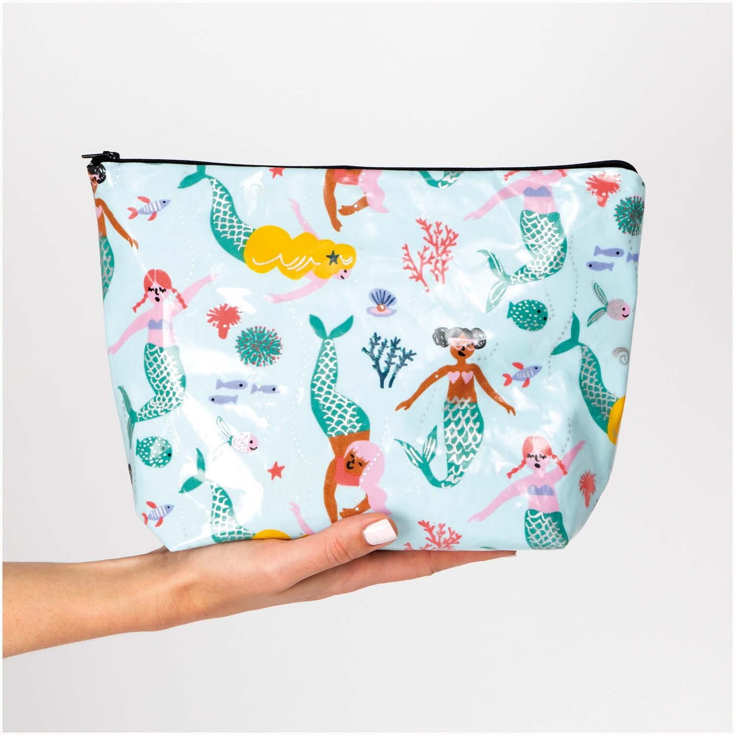 Druckstoff beschichtet Mermaid mit Meerjungfrauen-Muster auf einer Kosmetiktasche, gehalten von einer Hand.