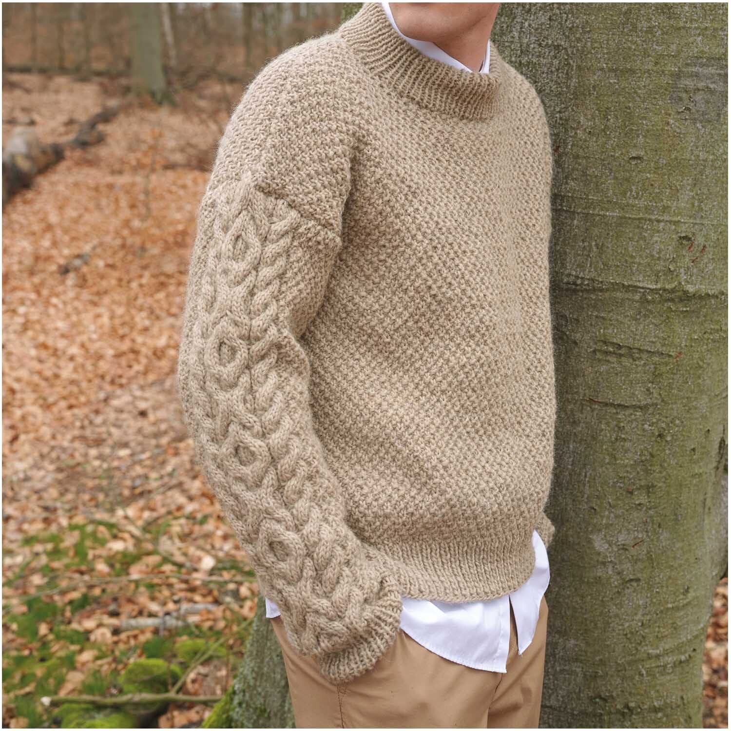 Essentials Organic Wool aran: Ein beiger Strickpullover mit Zopfmusterärmel, ideal für Herbstspaziergänge.