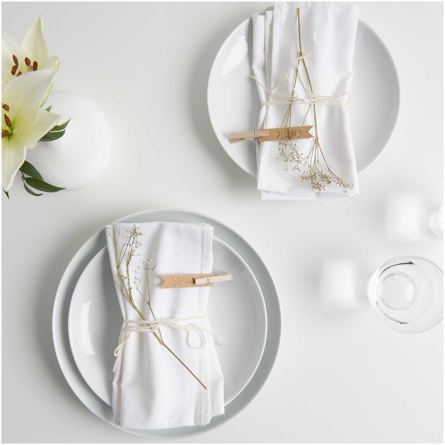 Stoffserviette 2 Stück weiß von Rico Design, elegant auf Tellern arrangiert mit Blumen und Kerzen.