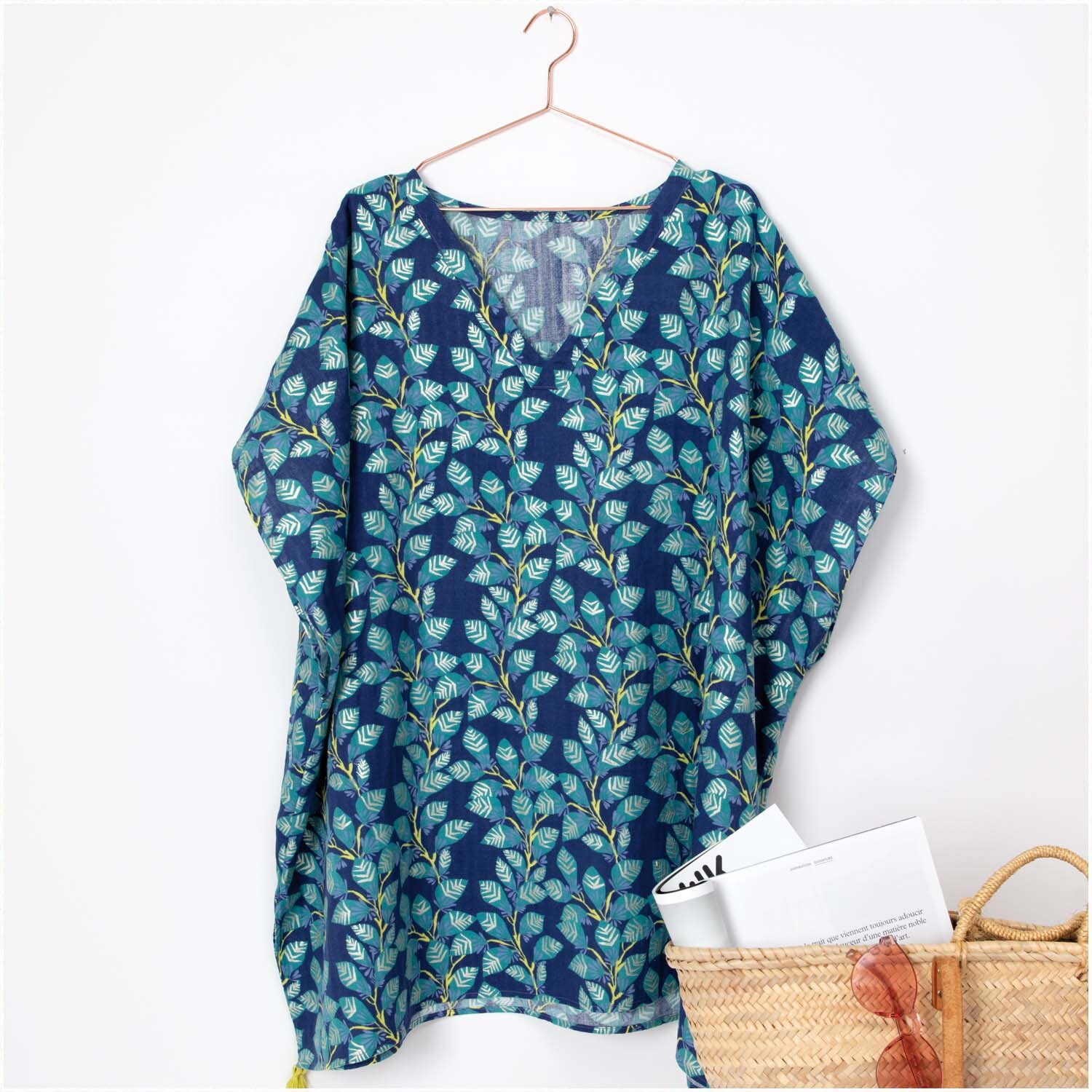 Musselin-Druckstoff Aloha Ranke Hot Foil 140cm zeigt ein blaues Kleid mit grünem Blattmuster, aufgehängt an einem Kleiderbügel.
