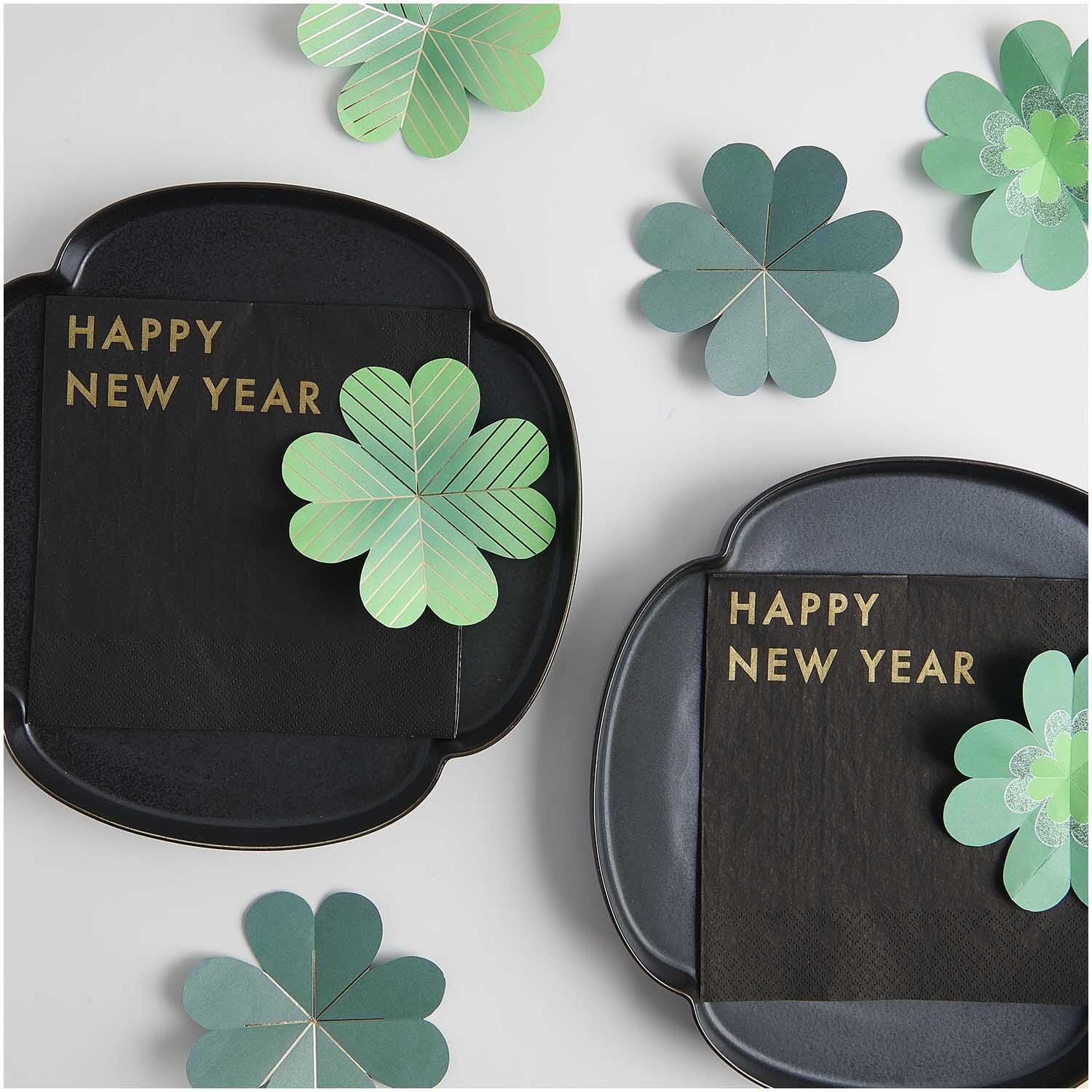 Paper Poetry Glücksklee aus Papier auf schwarzen Tellern mit "Happy New Year"-Schriftzug, dekorativ arrangiert.