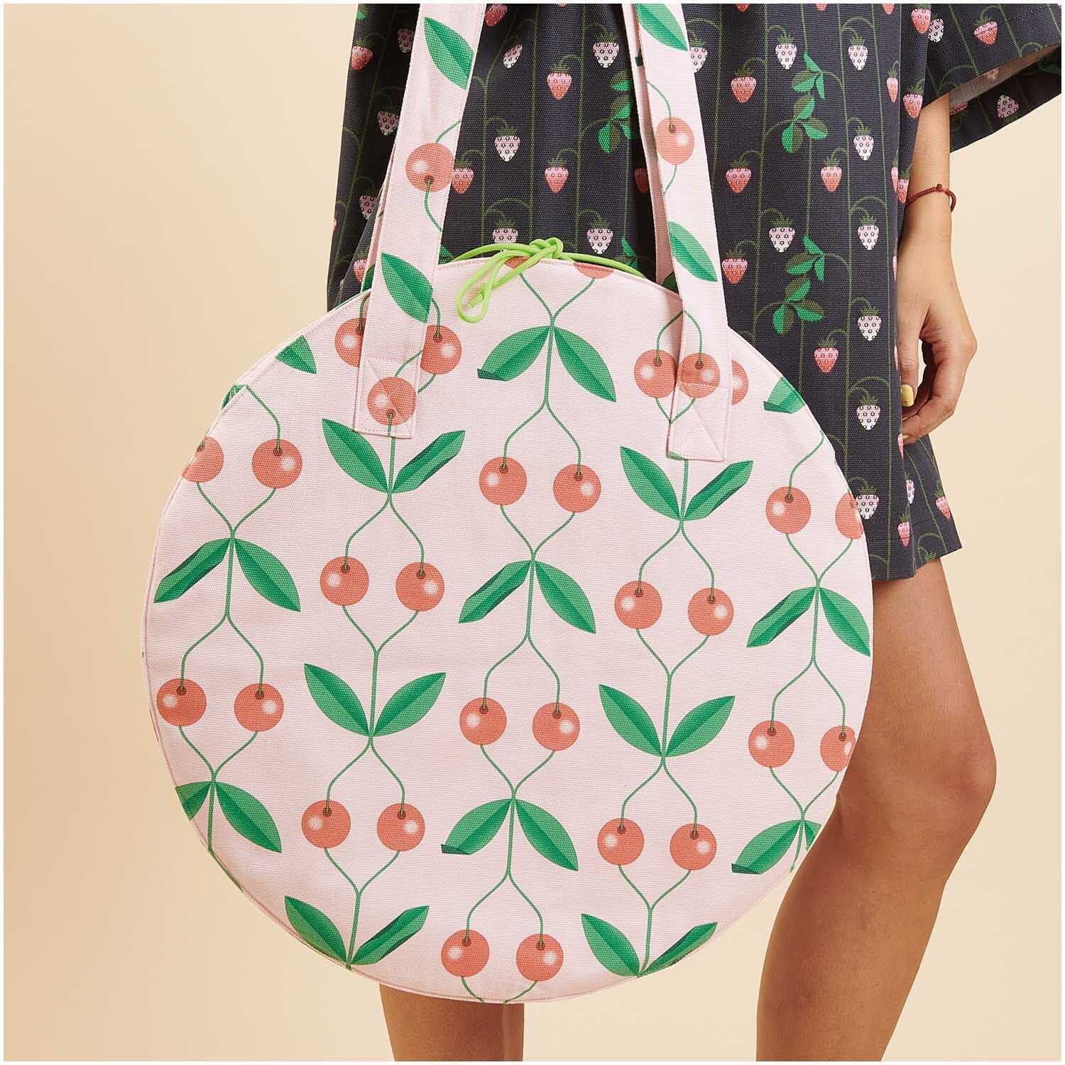 Meterware Canvas Kirschen rosa: Runde Tasche mit Kirschmuster, getragen von einer Person in gemustertem Kleid.