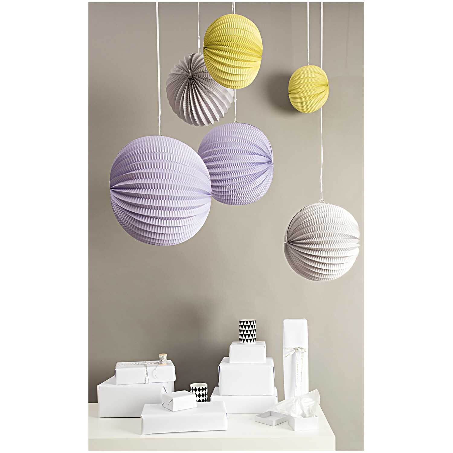 Lampions pastell 3 Stück von Rico Design: Hängende pastellfarbene Lampions in Gelb, Lila und Weiß über einem Tisch mit weißen Geschenken.