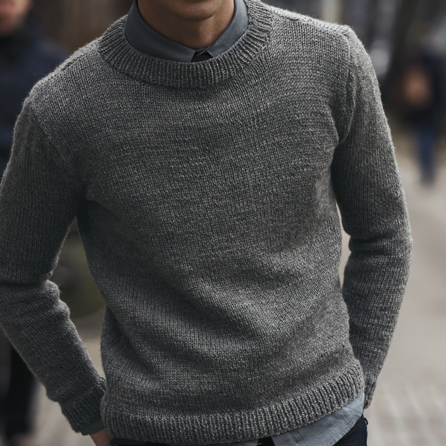 Strickanleitung Herrenpullover aus Essentials Soft Merino aran: Mann trägt grauen Pullover auf Straße.