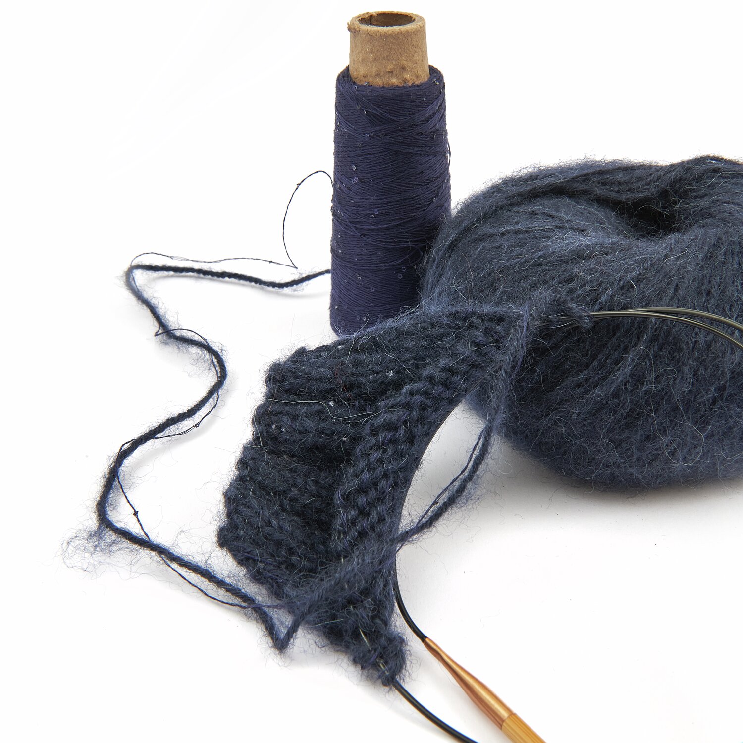 Dunkelblaues Strickgarn und Strickstück mit Stricknadeln, daneben eine Garnrolle. Ideal für kreative Strickprojekte. Perfekt für Handarbeitsliebhaber.