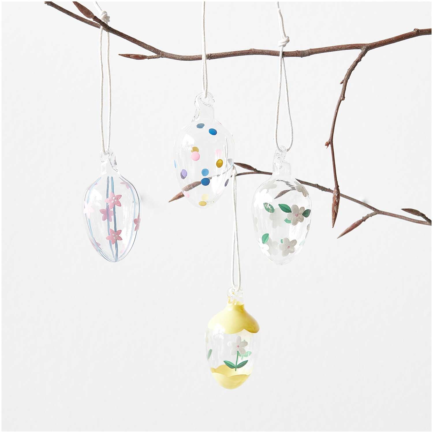 Glas Eier transparent handbemalt 4 Stück Ø 3cm von Rico Design hängen an einem Ast. Dekoriert mit bunten Mustern und Blumenmotiven.