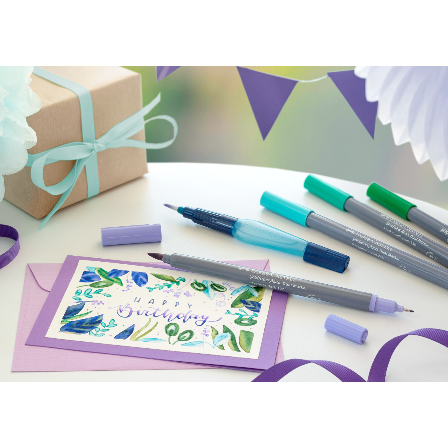 Goldfaber Aqua Dual Marker auf einem Tisch mit Geburtstagskarte, Geschenk und Dekorationen. Ideal für kreative Projekte.