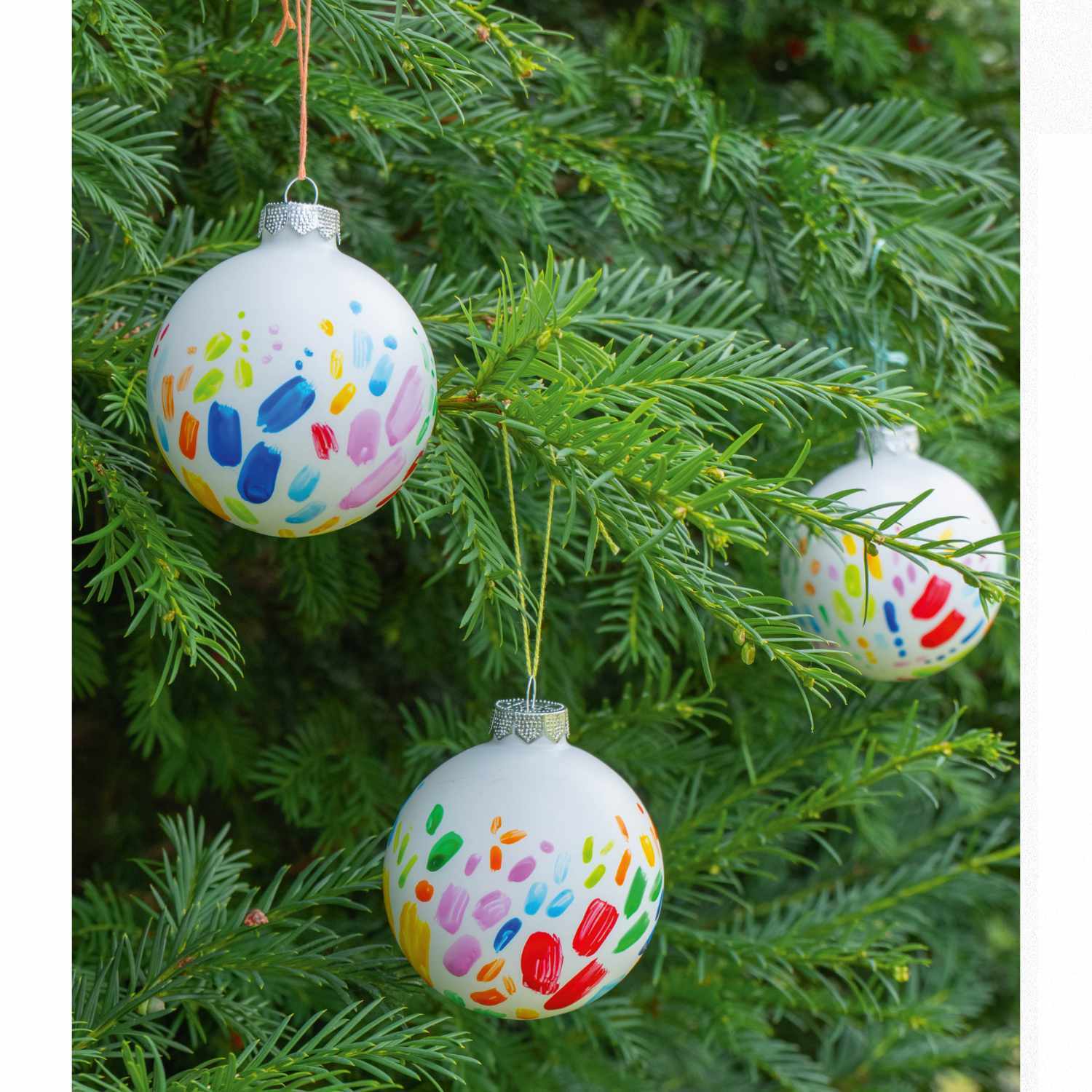 Porcelain & Glass Starterset matt: Drei bunte, handbemalte Kugeln hängen an einem grünen Tannenbaum.