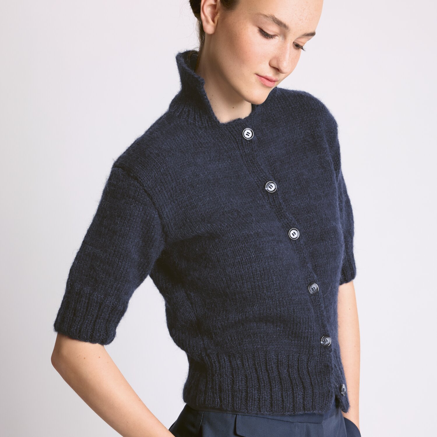 Strickset Jacke Modell 14 aus Luxury Knits: Dunkelblaue, kurzärmelige Strickjacke mit Knopfleiste, getragen von einer Frau.