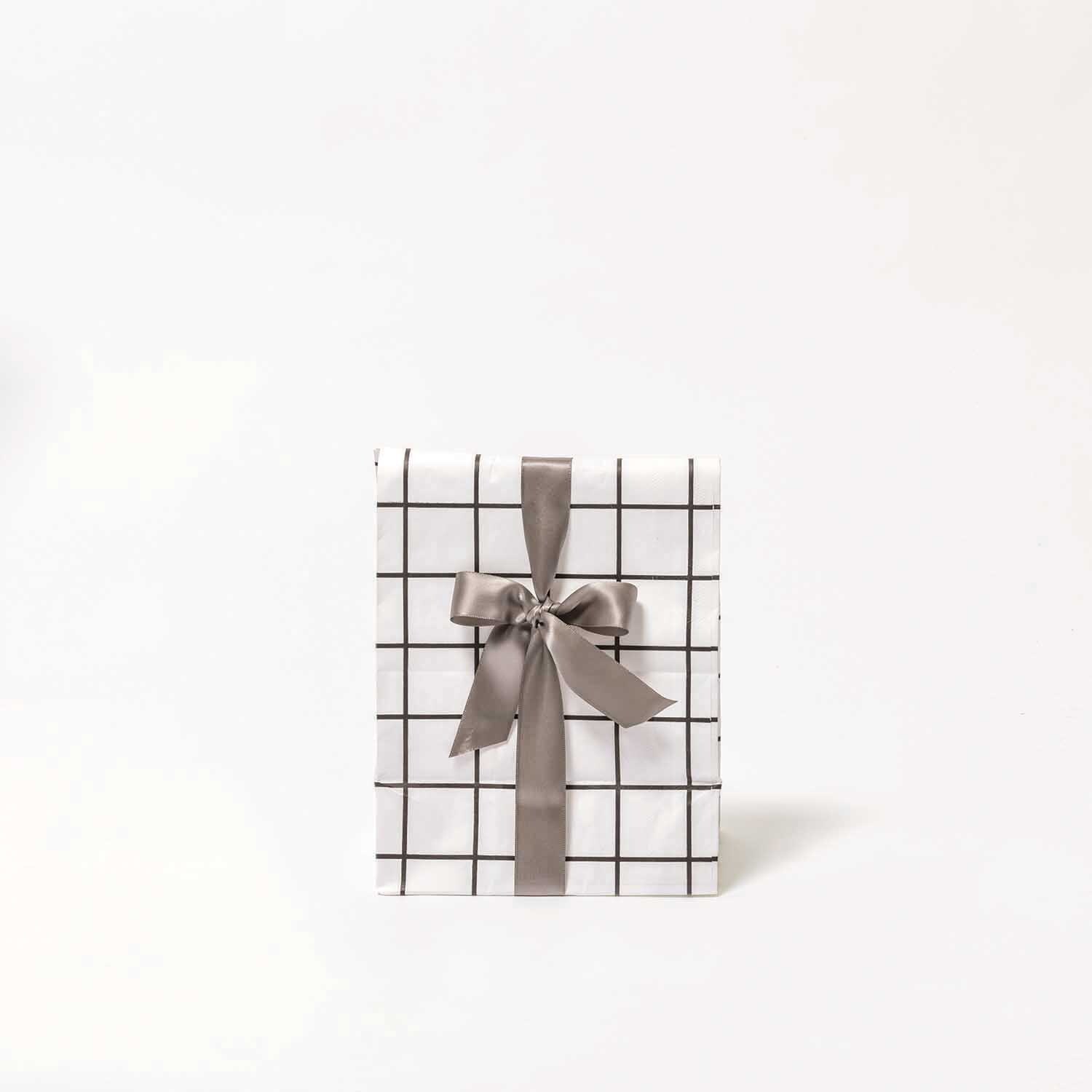 Paper Poetry Satinband 25mm 3m von Rico Design verziert ein Geschenk mit grauem Schleifenband auf kariertem Papier.