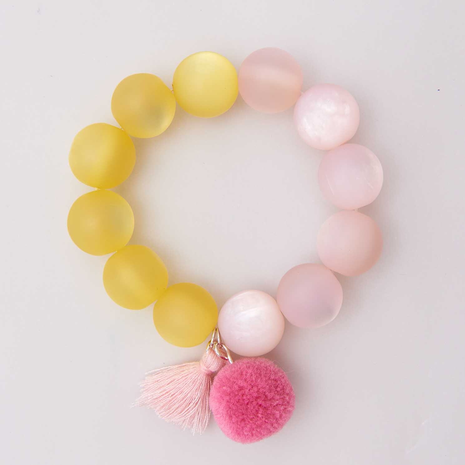 Quasten mit Öse 2,2cm 2 Stück von Rico Design in Rosa, dekoriert mit bunten Perlen auf einem Armband.