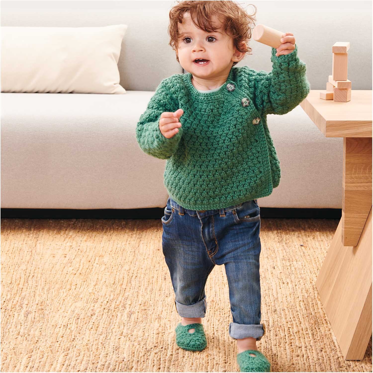 Rico Baby Dream dk uni - A Luxury Touch: Kleinkind in grünem Strickpullover spielt im Wohnzimmer.