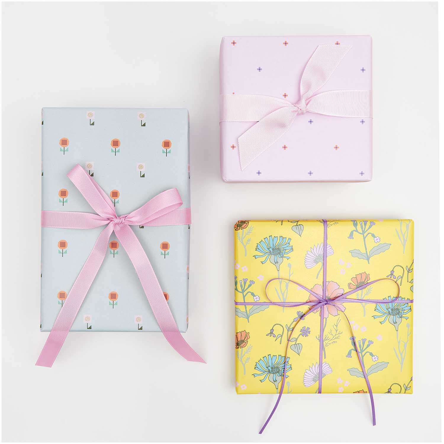 Geschenkpapier Blumen Rosa: Drei Geschenke in rosa, blau und gelb mit floralen Mustern und Schleifen.