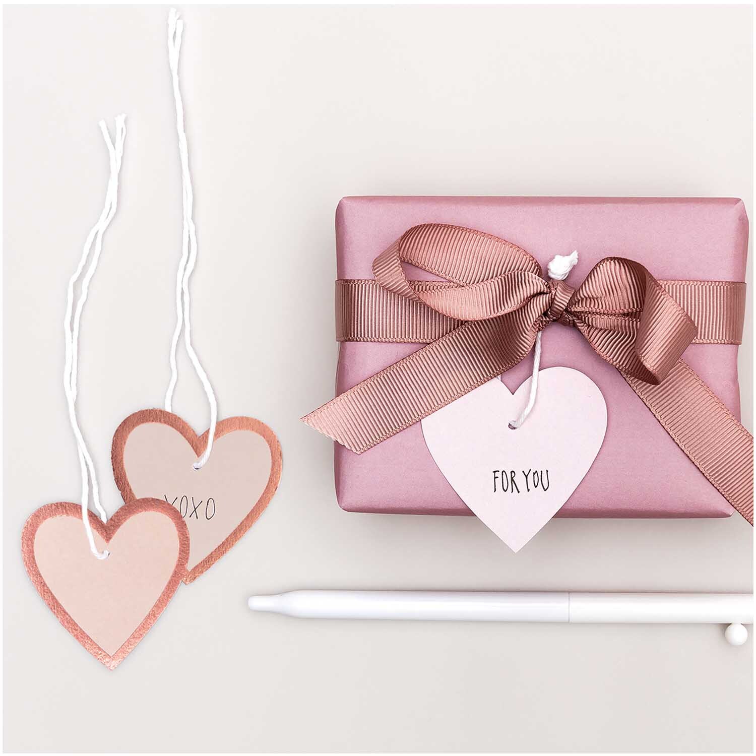 Paper Poetry Papieranhänger Herzen M 24 Stück in Puder-Roségold neben Geschenk mit Schleife.