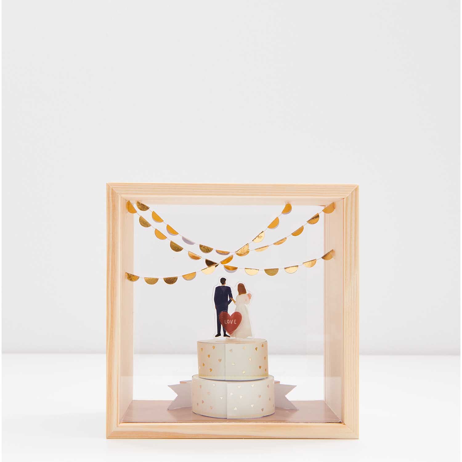 Figurico Gelsticker Hochzeit 1: Hochzeitstorte mit Brautpaar in Holzrahmen, goldene Girlanden.