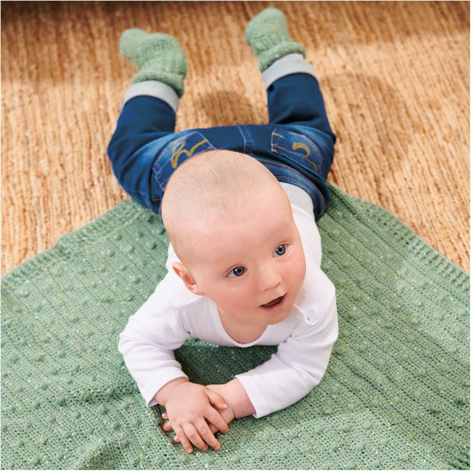 Rico Baby Dream Tweed dk - A Luxury Touch: Ein Baby liegt auf einer moosgrünen Decke von Rico Design.