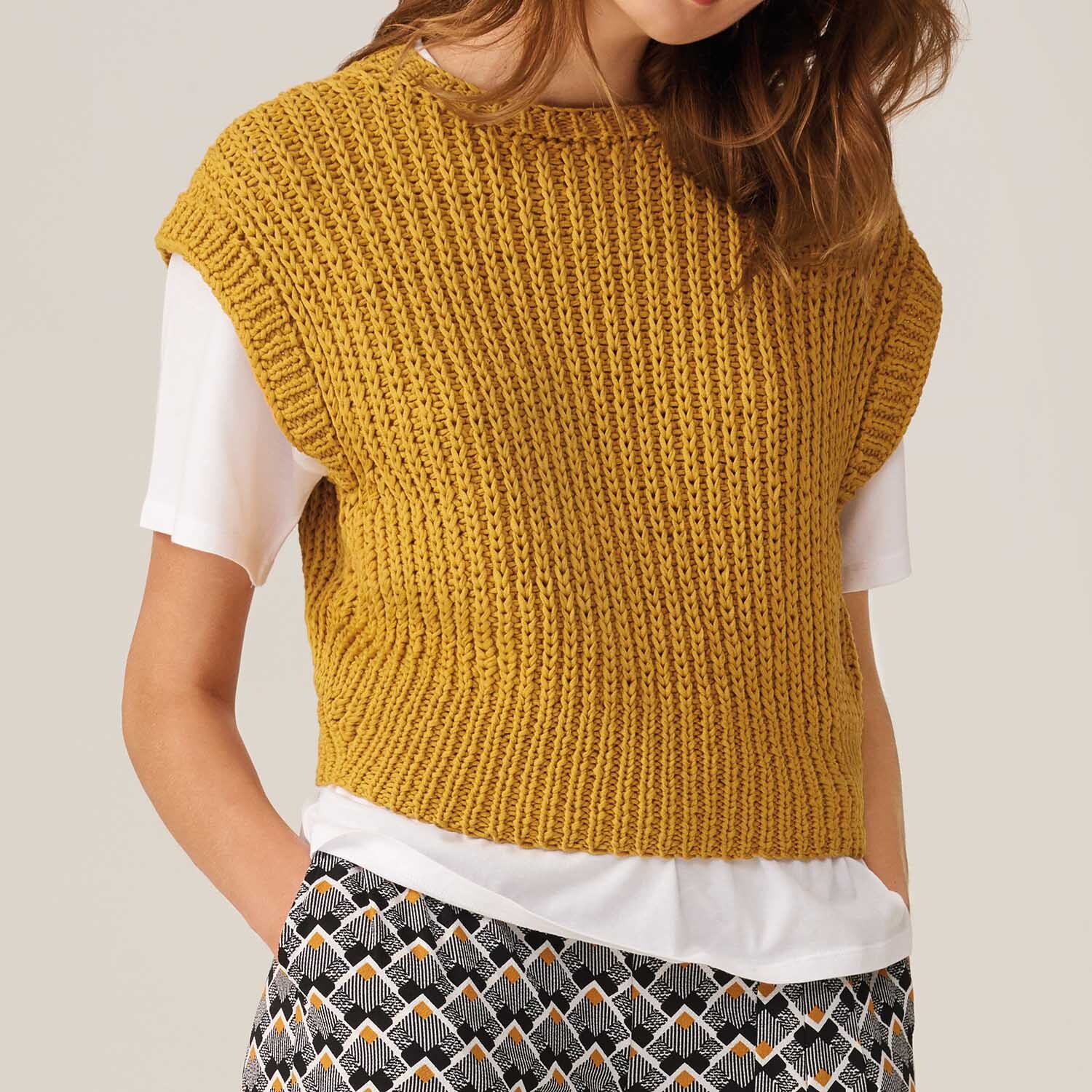 Strickanleitung Top aus Fashion Cotton Ribbon chunky: Frau trägt gelbes Stricktop über weißem T-Shirt, kombiniert mit gemusterten Hosen.