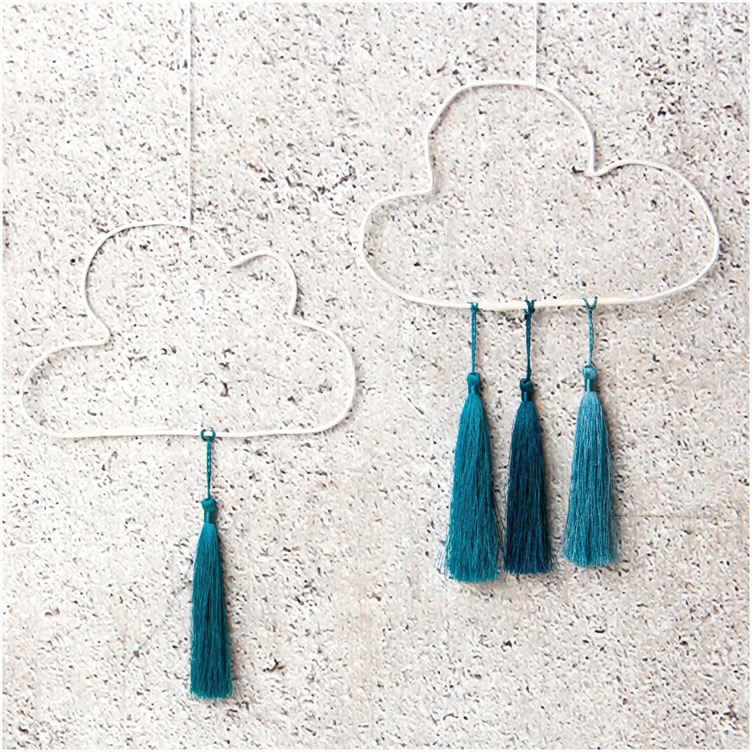 Quasten fein 9cm 5 Stück: Zwei Wolken-Dekorationen mit aqua Quasten an einer Steinwand.