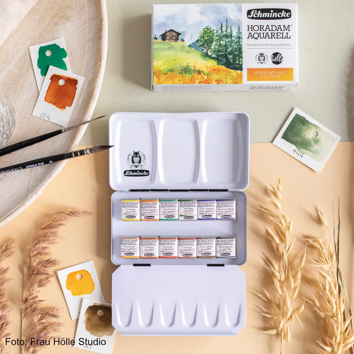 Schmincke Horadam Aquarellkasten mit 12 halben Näpfen, Pinsel und Farbkarten auf hellem Tisch.
