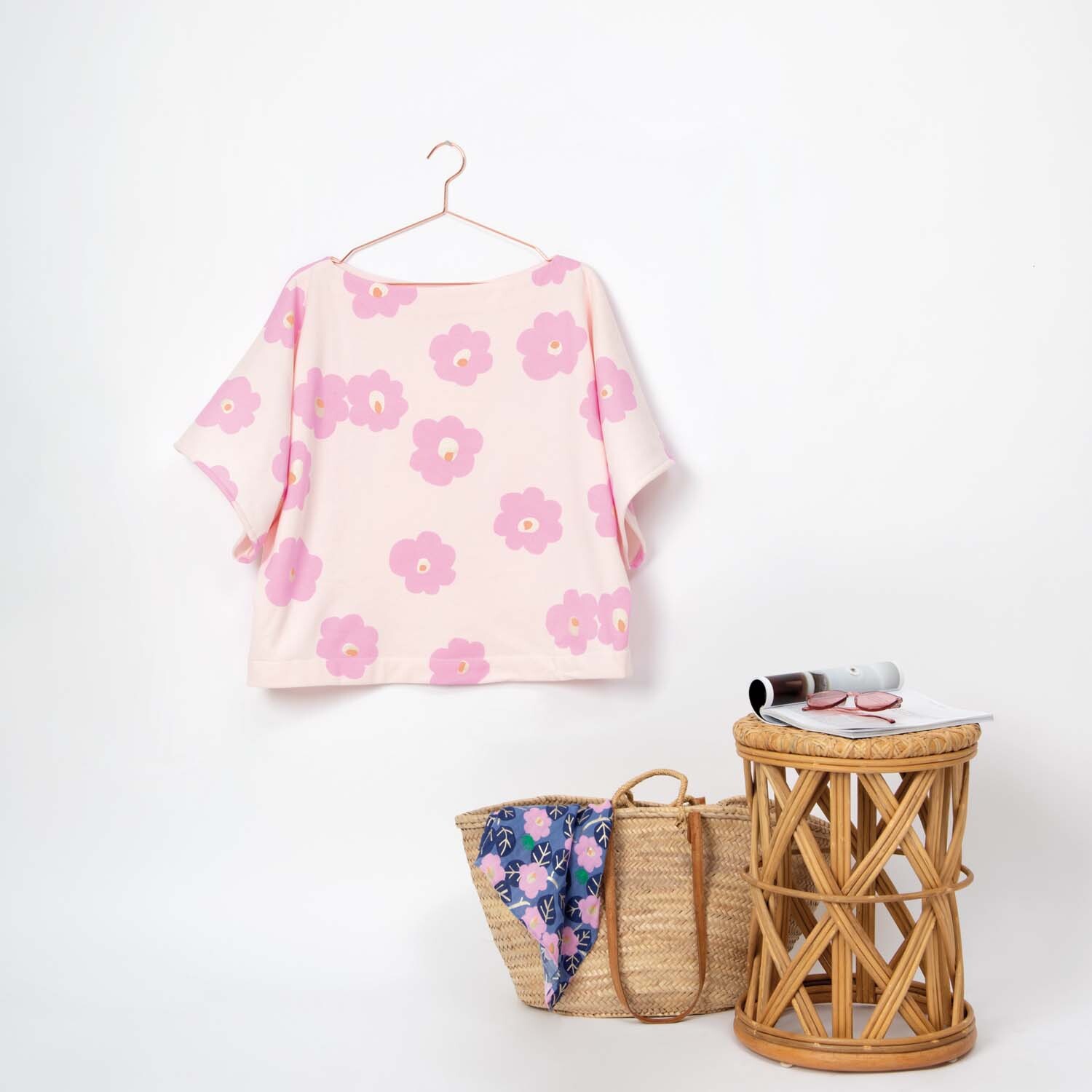 Sweatshirt-Stoff mit Aloha-Blumenmuster in Rosa, aufgehängt neben einem Korb und Tisch. Marke: Rico Design.