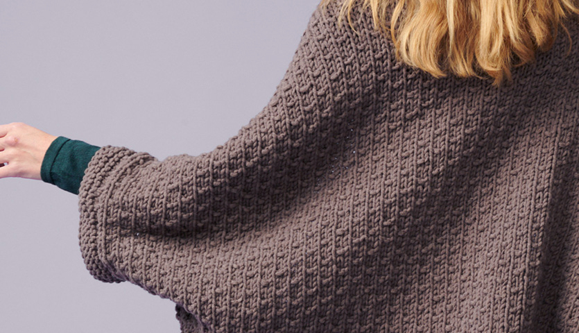 Strickanleitung Poncho aus Polar: Frau trägt braunen, gestrickten Poncho mit feinem Muster, ideal für kühle Tage.