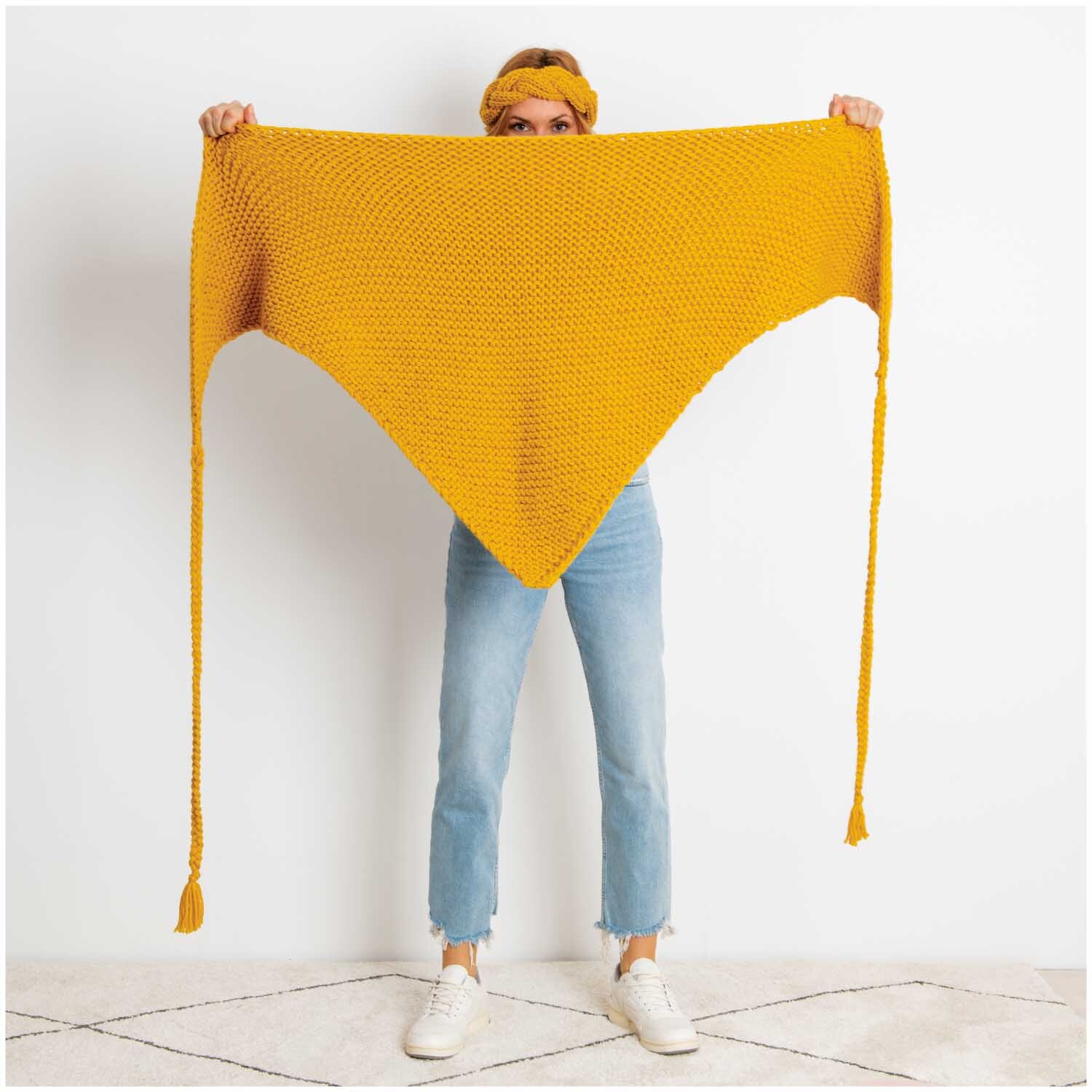Essentials Mega Wool chunky: Person hält ein großes, senffarbenes Stricktuch von Rico Design.