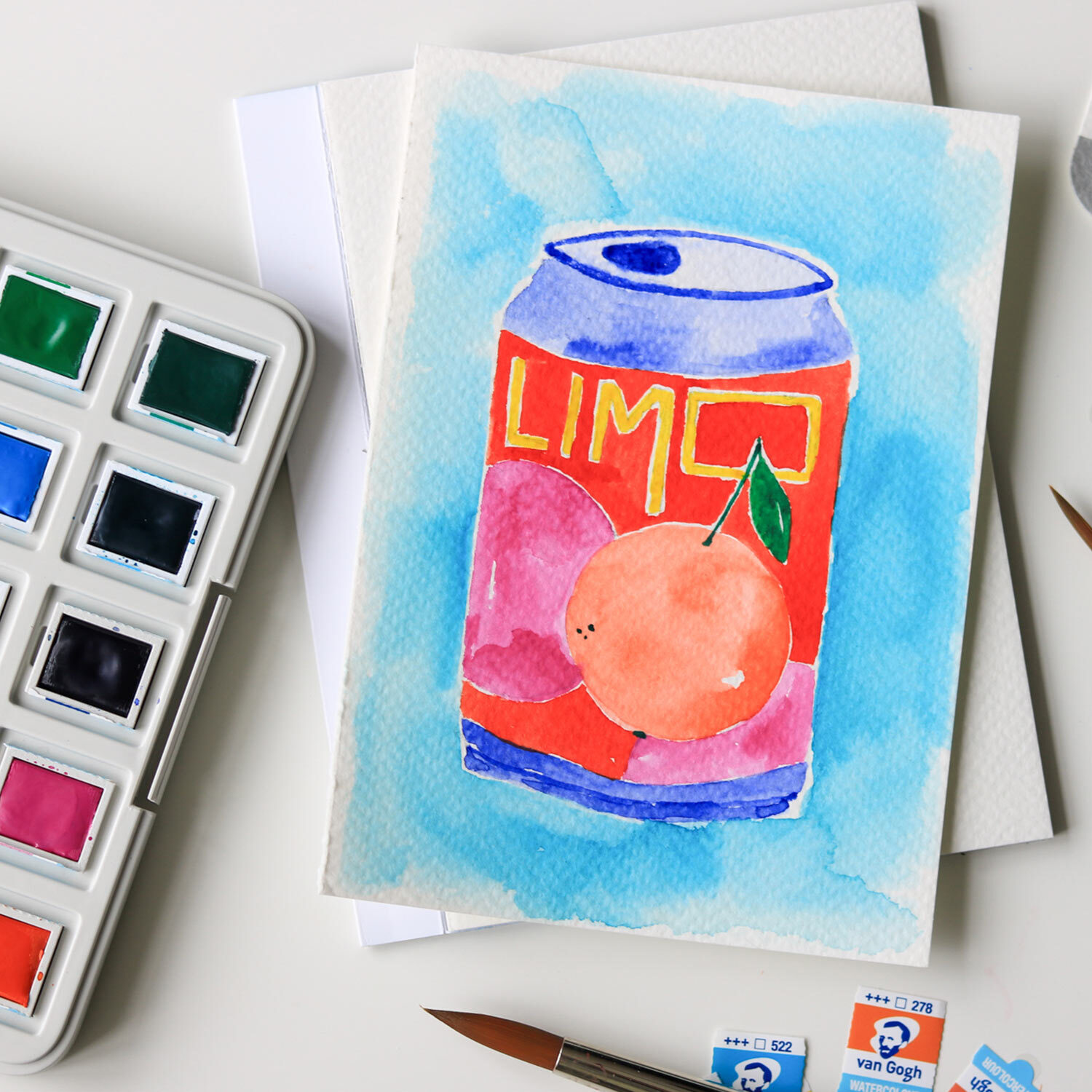 Aquarell Set intensive Farben 12 Näpfchen: Gemaltes Limonadenmotiv mit Pfirsich, umgeben von Farbnäpfchen und Pinseln.