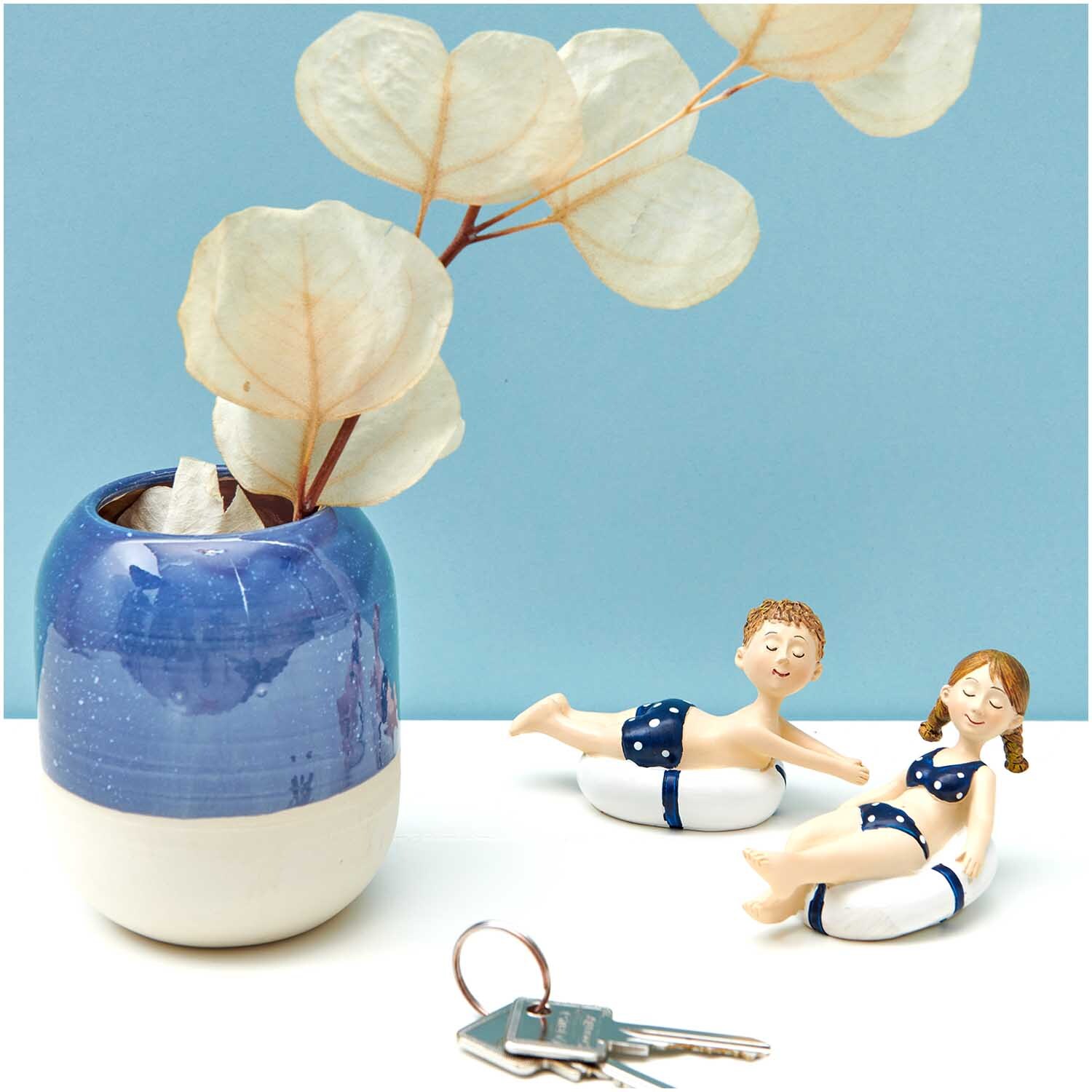 Deko-Figur Mädchen mit Schwimmreifen 9x6cm von Rico Design neben blauem Keramiktopf mit Pflanze.