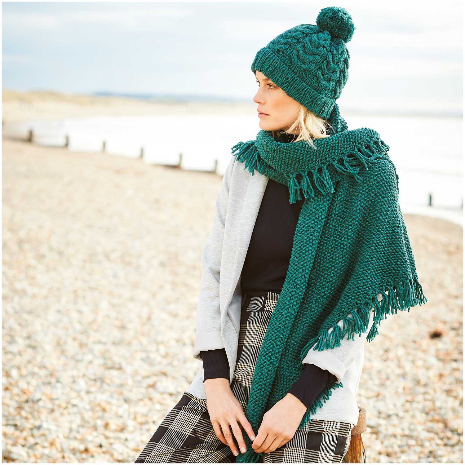 Essentials Alpaca Blend chunky Schal und Mütze in Alge von Rico Design, getragen von Frau am Strand.