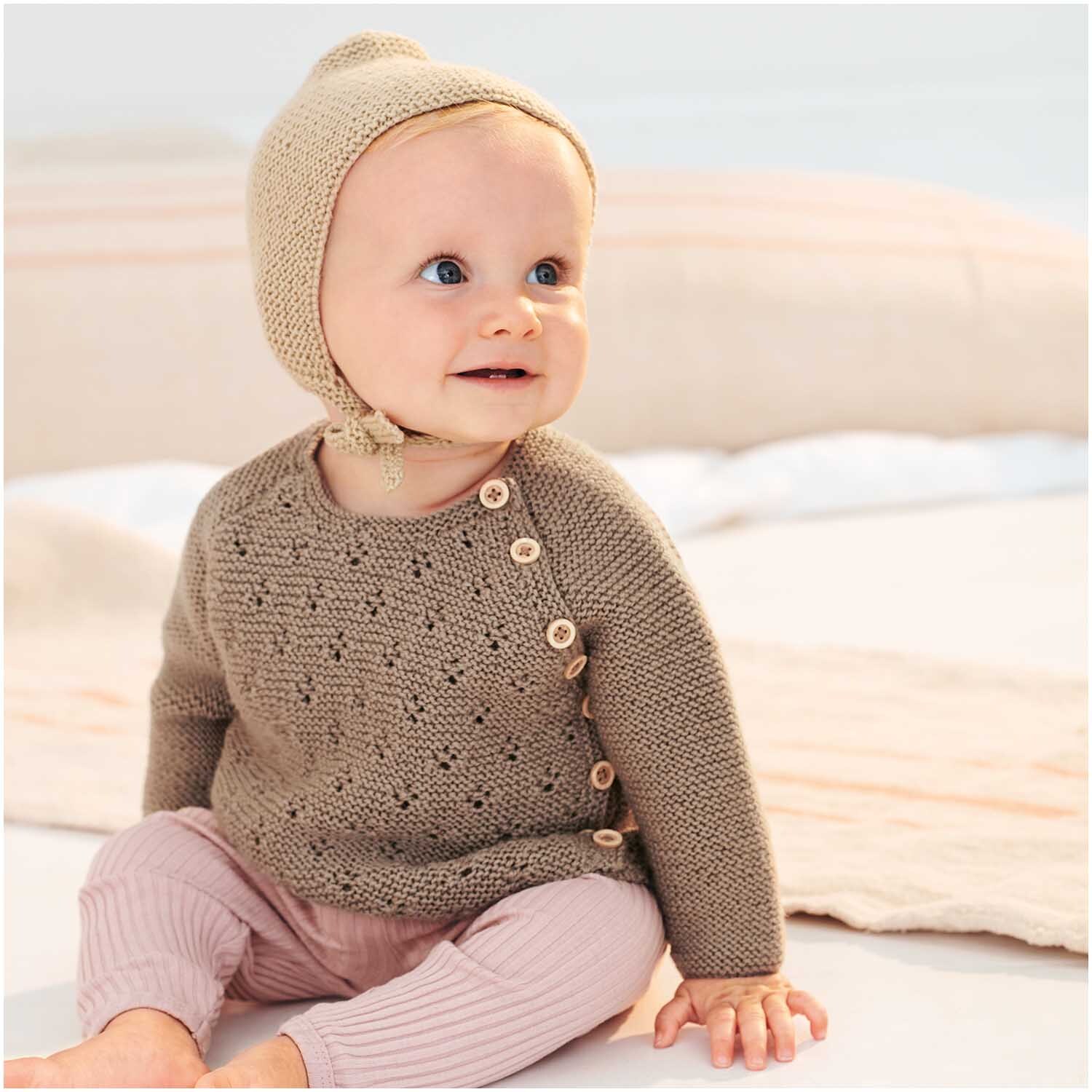Baby Merino: Ein lächelndes Baby in gestricktem Outfit mit Mütze, aus weicher Wolle von Rico Design.