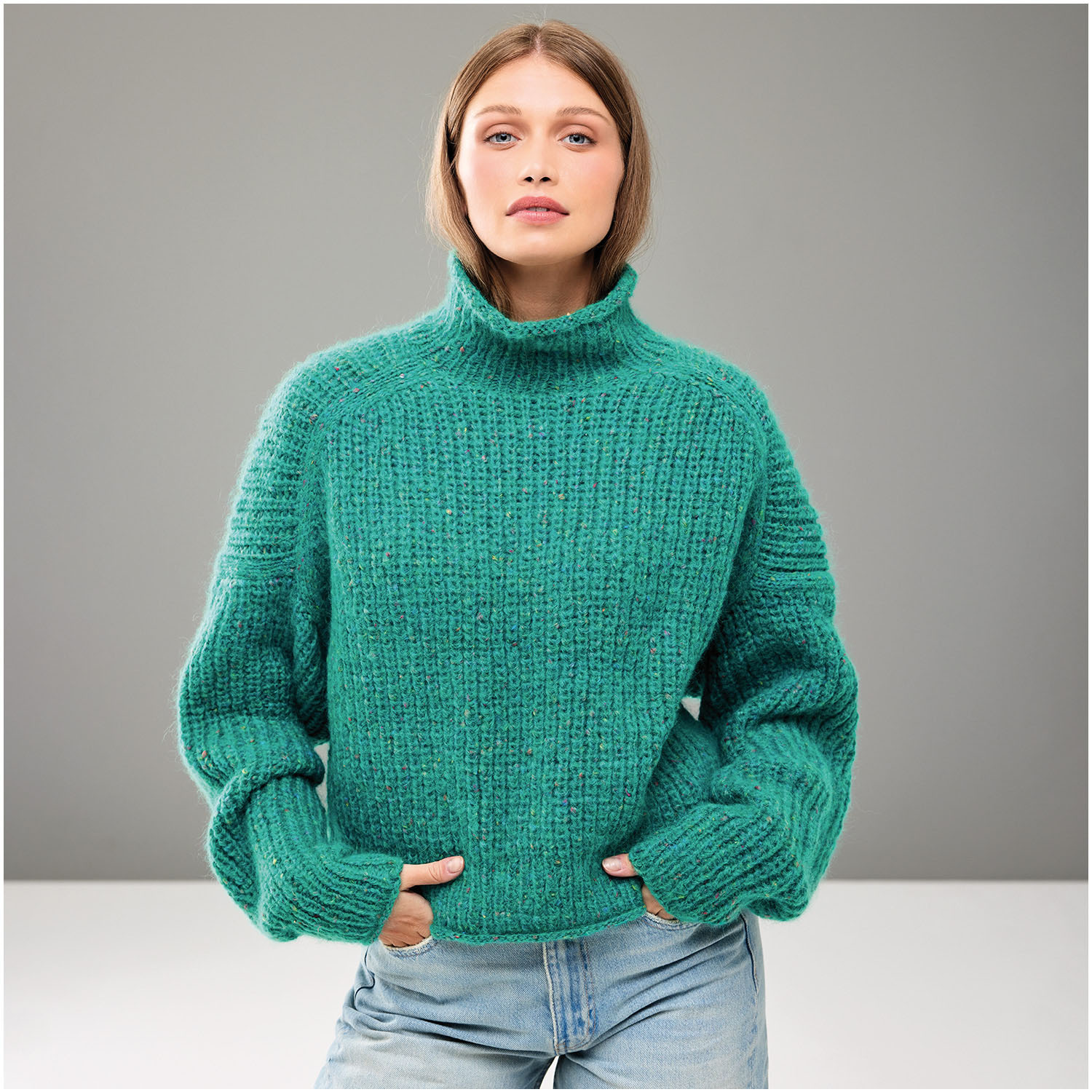 Strickset Pullover Modell 23: Frau trägt grünen Rollkragenpullover, kombiniert mit blauen Jeans.