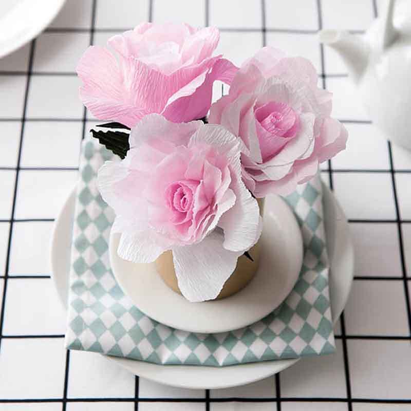 Floristenkrepp von Rico Design: Zarte rosa und weiße Papierblumen in einer Vase auf kariertem Tuch.