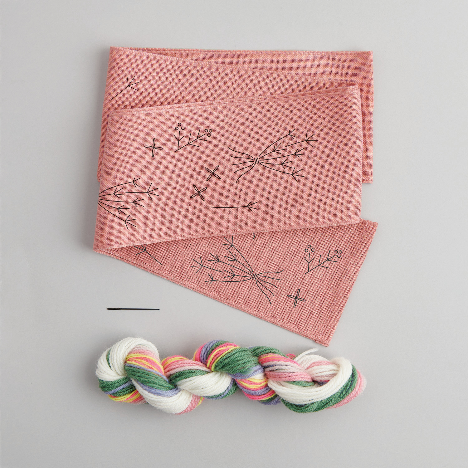 Stickpackung Schleife Frühlingsblümchen vorgezeichnet von Rico Design zeigt rosa Stoff mit Blumenmuster und bunte Stickgarn.