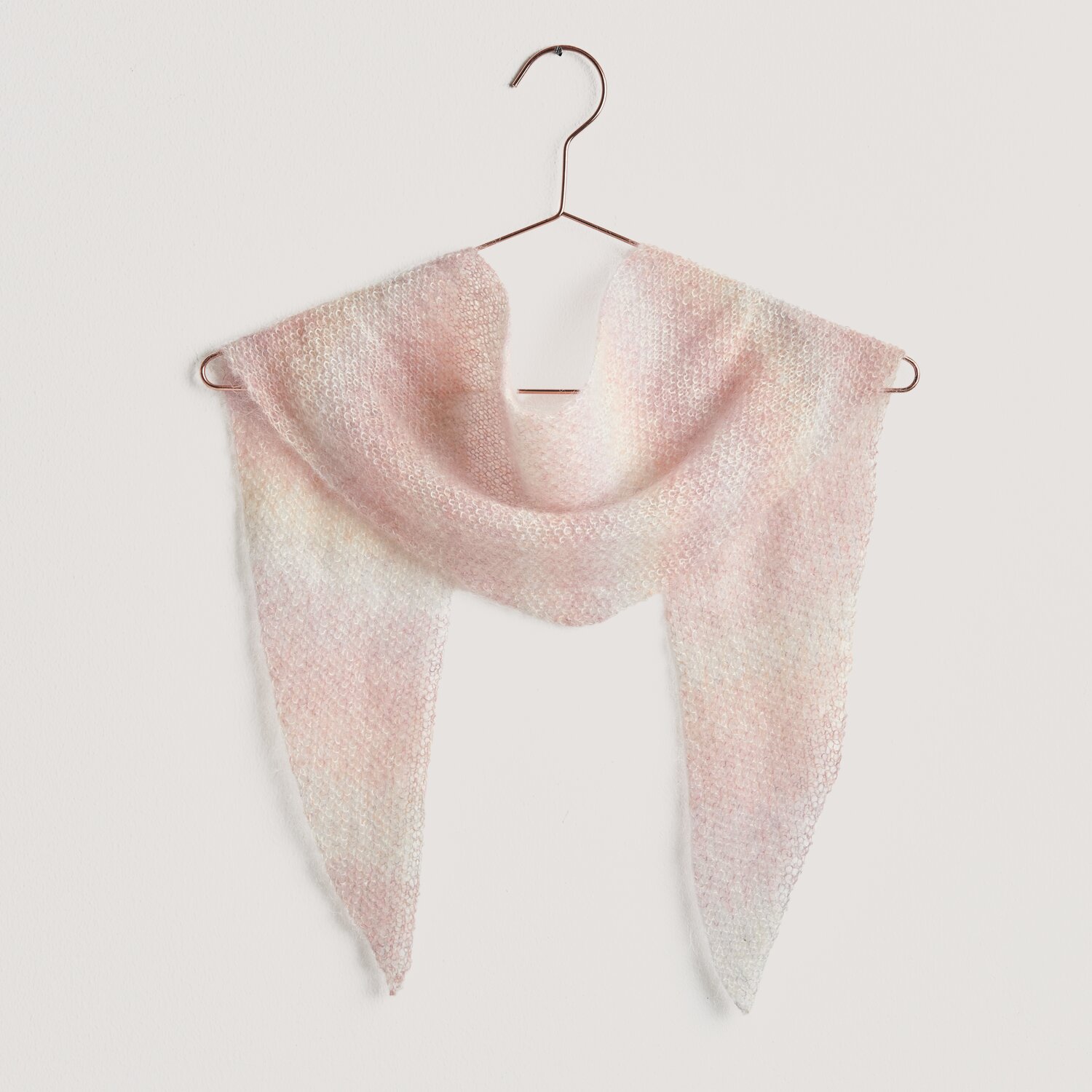 Strickset Mini-Dreieckstuch Modell 15a aus Lovewool No. 20, zartes Pastell-Dreieckstuch von Rico Design, aufgehängt an einem Kleiderbügel.