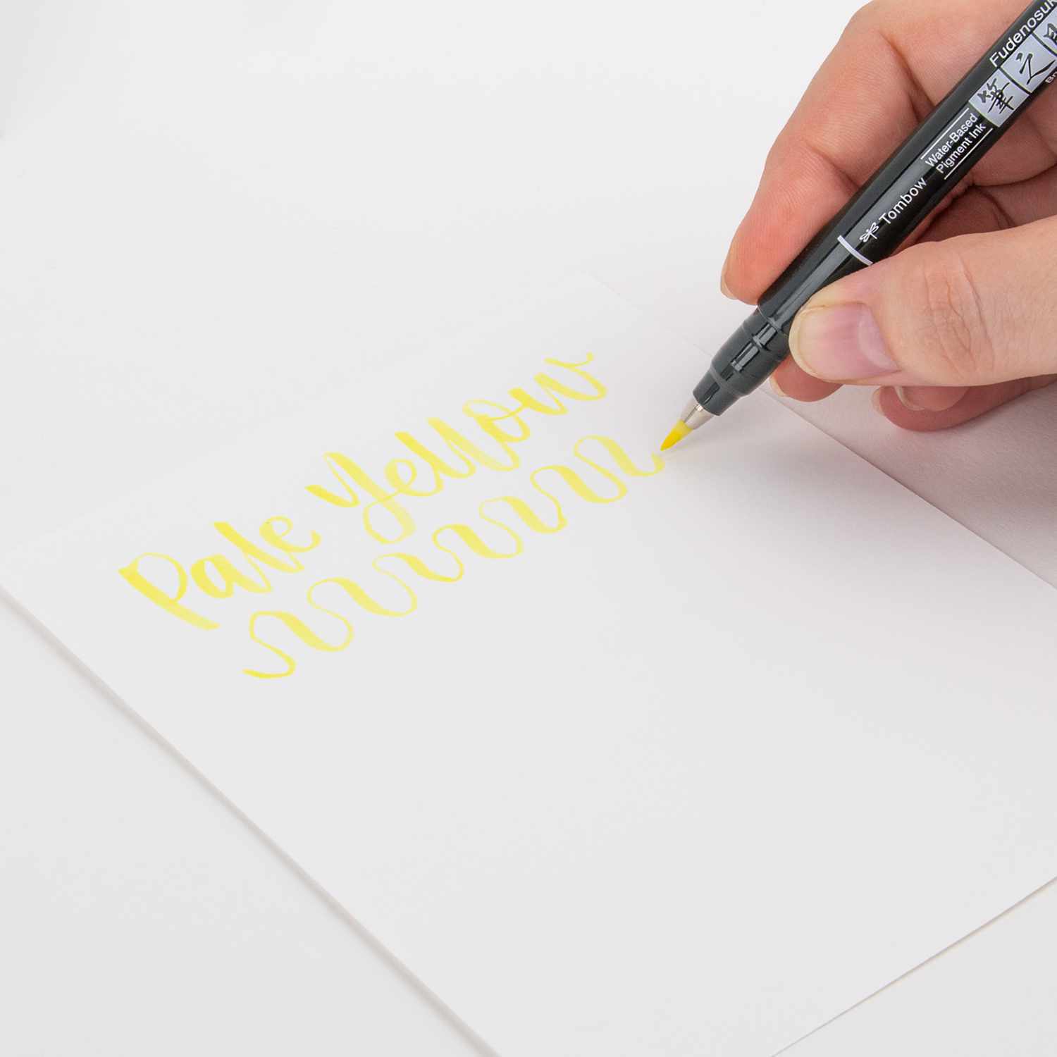 Fudenosuke Brush Pen Pastel schreibt in blassem Gelb auf weißem Papier, gehalten von einer Hand.