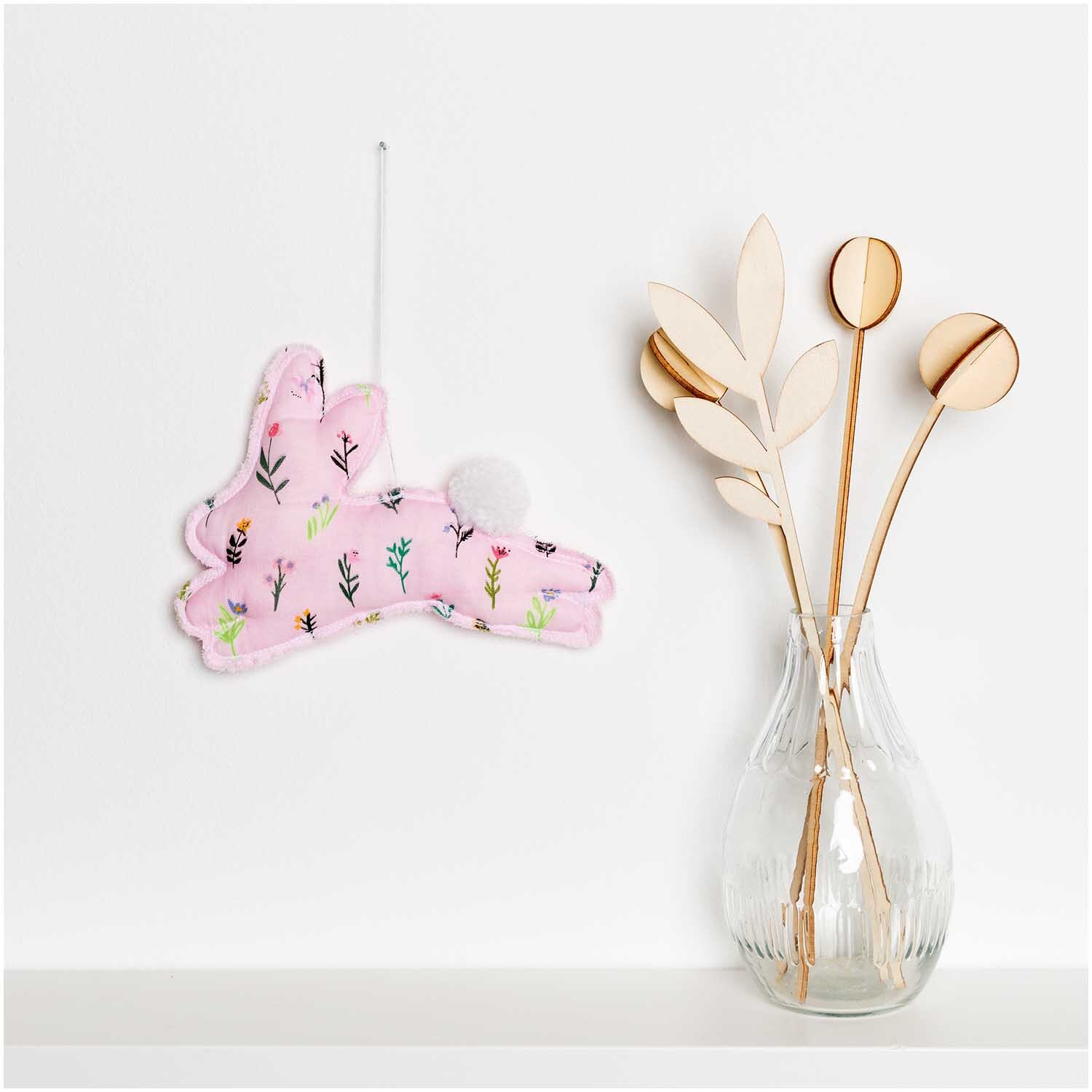 Musselin-Druckstoff Bunny Hop mit Streublumen in Rosa, dekoriert neben einer Vase mit Zweigen.