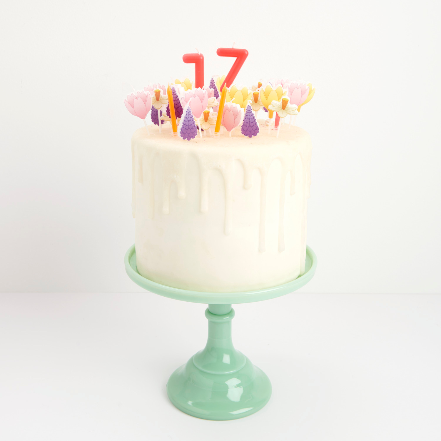 Kerzen Osterglocken: Weißer Kuchen mit bunten Blumenkerzen und roten Zahlen auf grünem Teller.