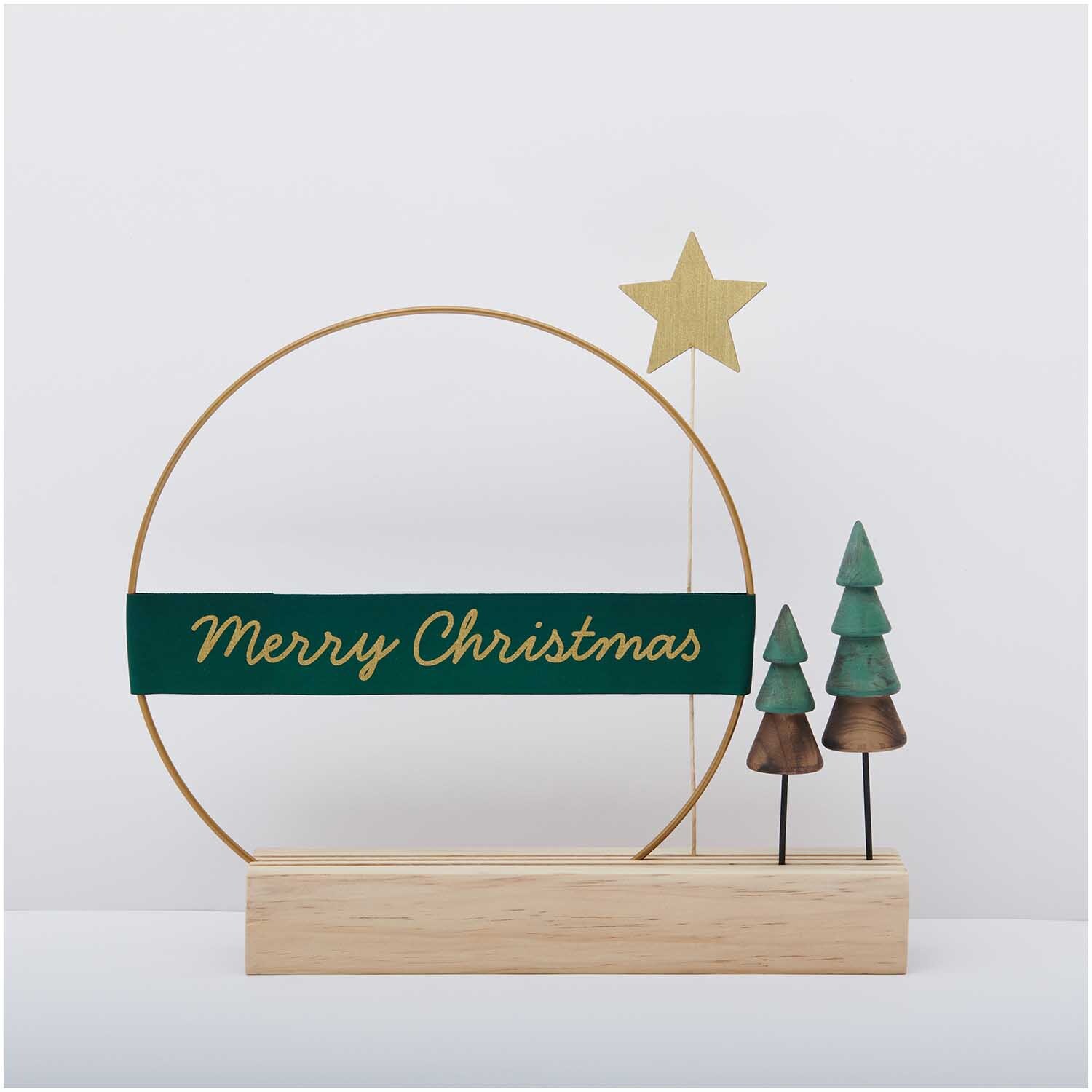 Paper Poetry Taftband Merry Christmas: Dekoratives grünes Band mit goldener Schrift, Holzständer und kleinen Tannenbäumen.
