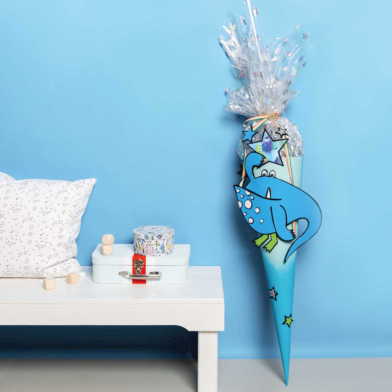 Bastelanleitung Monster-Schultüte für Jungen: Eine blaue Schultüte mit Monster-Motiv, dekoriert mit Sternen, steht neben einem weißen Tisch.