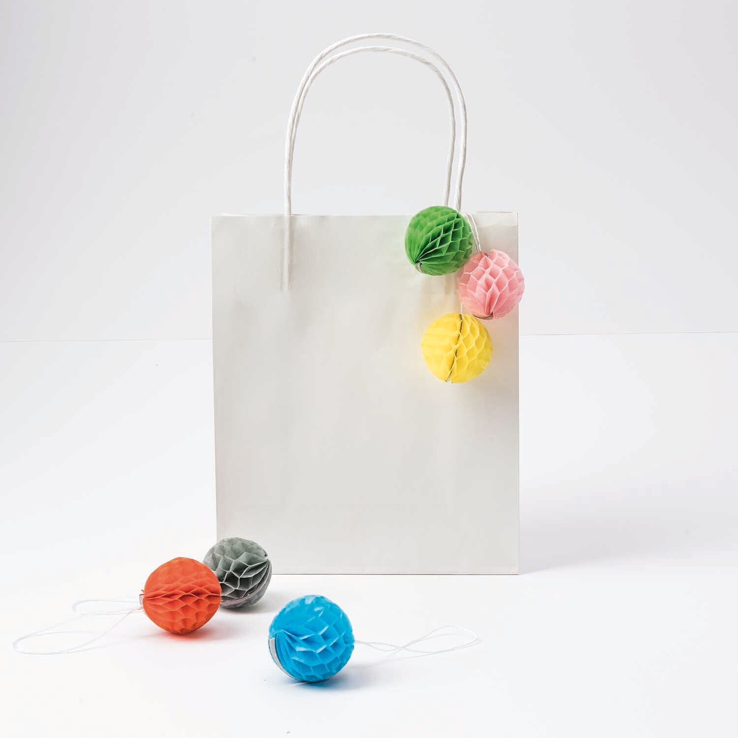 Mini-Wabenbälle 4cm 6 Stück von Rico Design in verschiedenen Farben, dekorativ an einer weißen Geschenktüte befestigt.