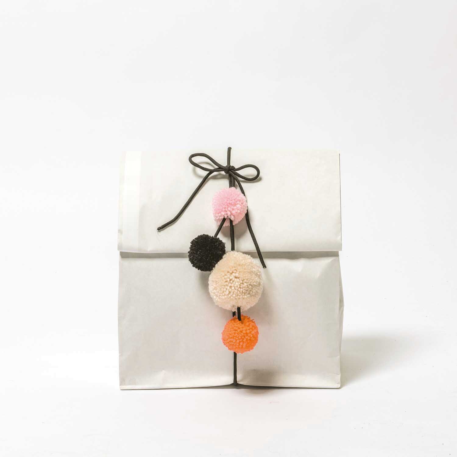 Garn Pompons 24 Stück: Weiße Tüte mit bunten Pompons in Rot, Orange und Schwarz von Rico Design.